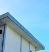 A modern building with a flat roof and a light blue sky in the background. The structure features a clean, minimalist design with a visible gutter system along its edge.