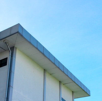 A modern building with a flat roof and a light blue sky in the background. The structure features a clean, minimalist design with a visible gutter system along its edge.